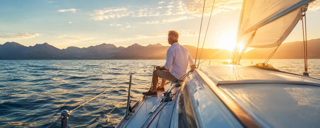 Man sailing toward mountains at sunset