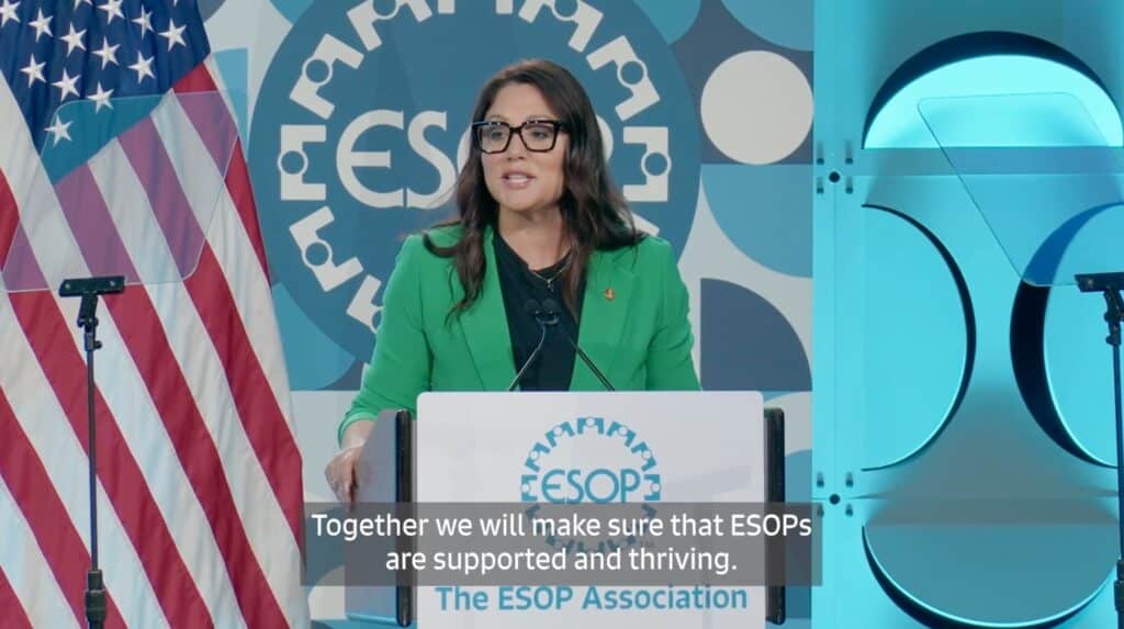 Secretary of Labor Lori Chavez-DeRemer delivering a keynote at The ESOP Association event, standing at a podium with an American flag and ESOP Association logo in the background.