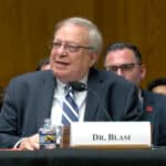 Dr. Joseph Blasi speaking into a microphone during a U.S. Senate HELP Committee hearing, seated beside other attendees.